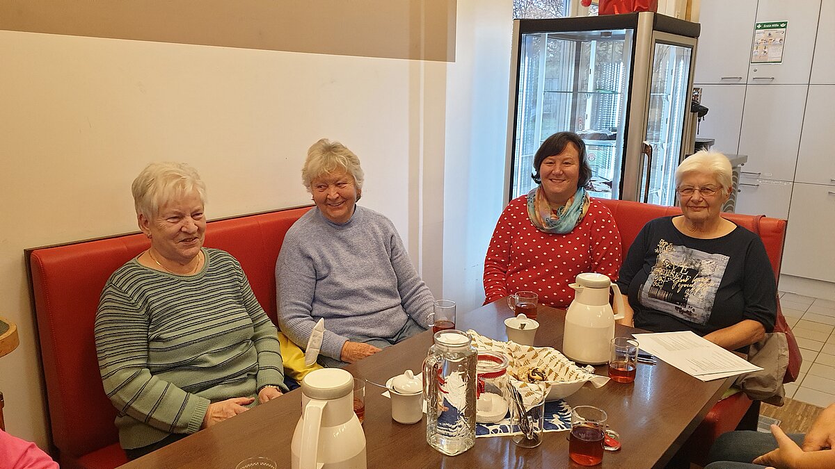 Vier ältere Damen sitzen gemeinsam an einem Tisch, auf denen Kaffeetassen und Kuchen stehen.