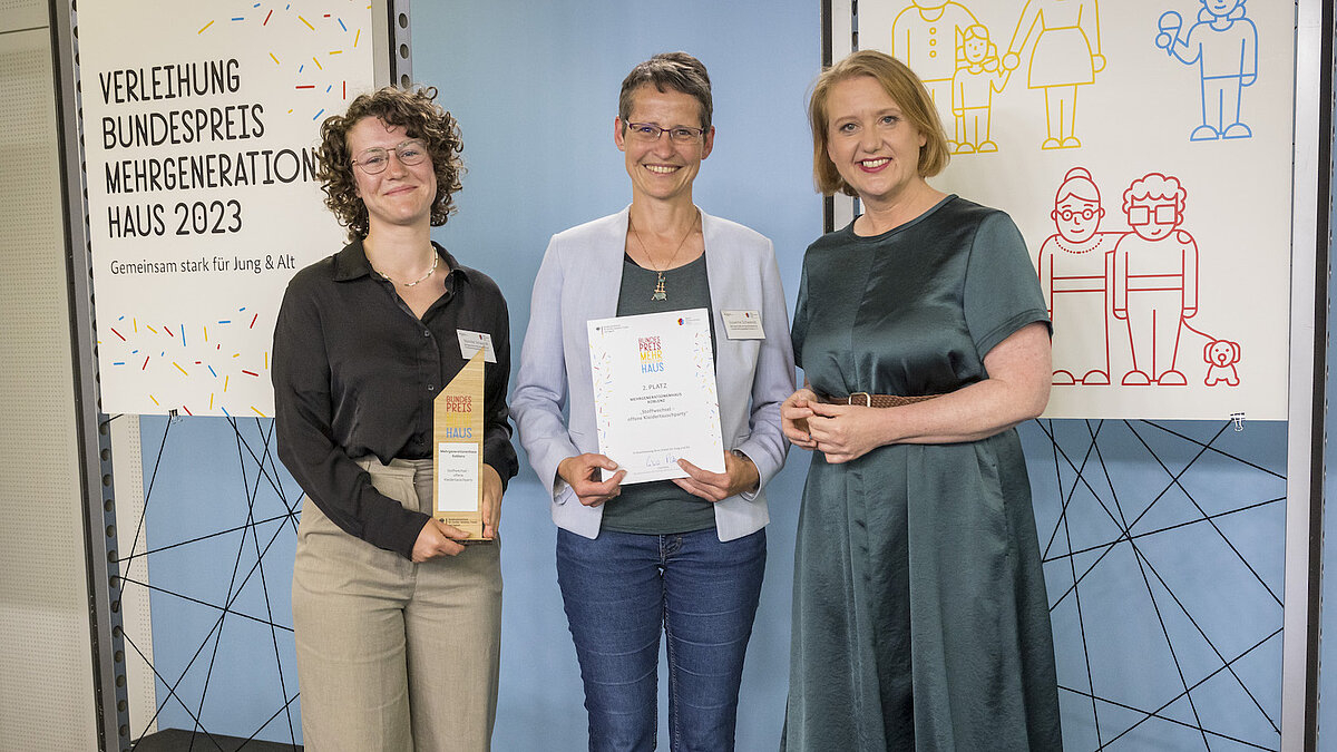 Drei Frauen stehen auf einer Bühne und lächeln in die Kamera.