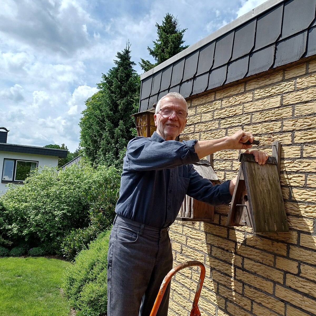 Christoph Godzik bringt ein Vogelhaus an einer Wand an.