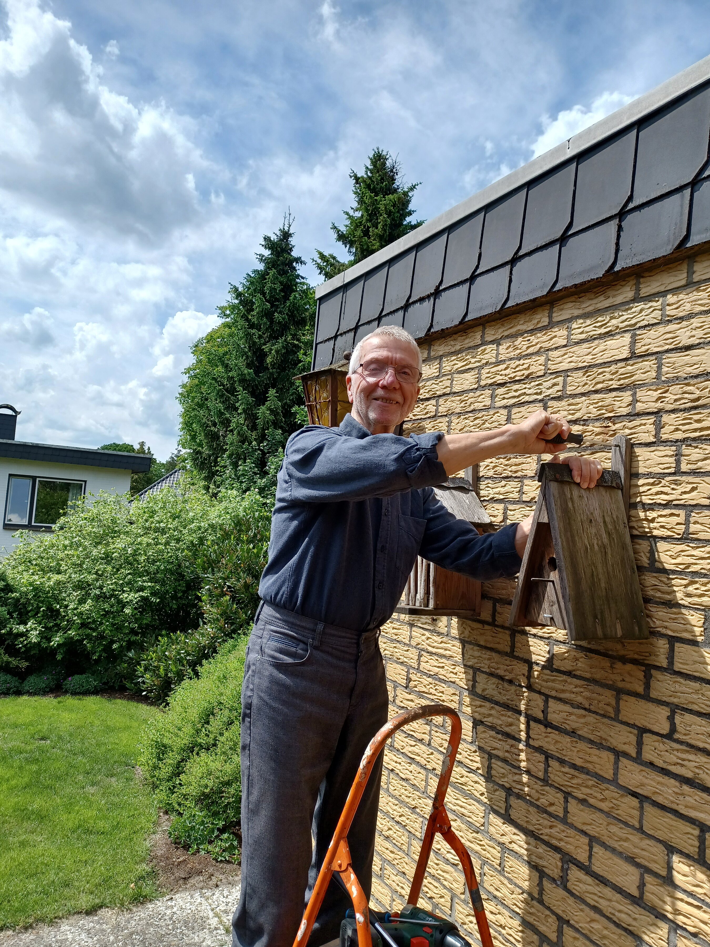 Christoph Godzik bringt ein Vogelhaus an einer Wand an.