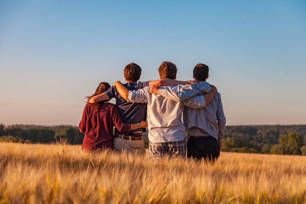 Vier Jugendliche, die sich an den Schultern fassen, auf einem Feld im Abendlicht